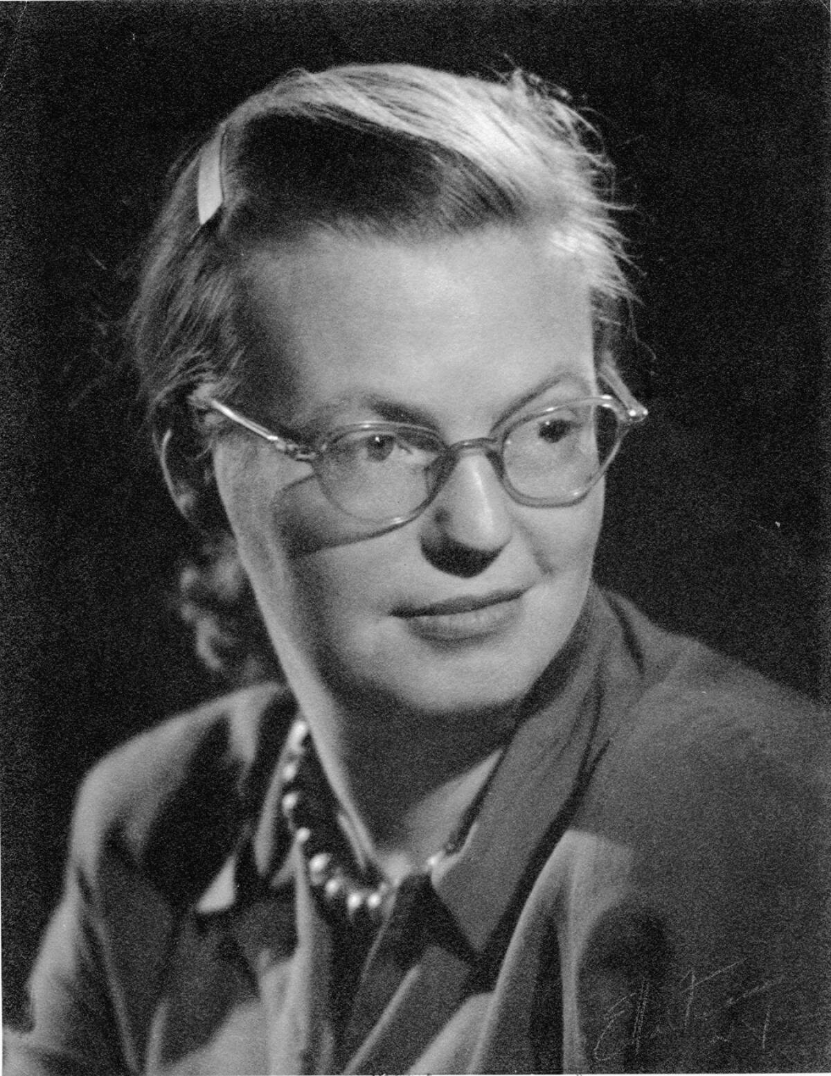 A black-and-white portrait of author Shirley Jackson, wearing glasses and pearls with a button-down blouse.