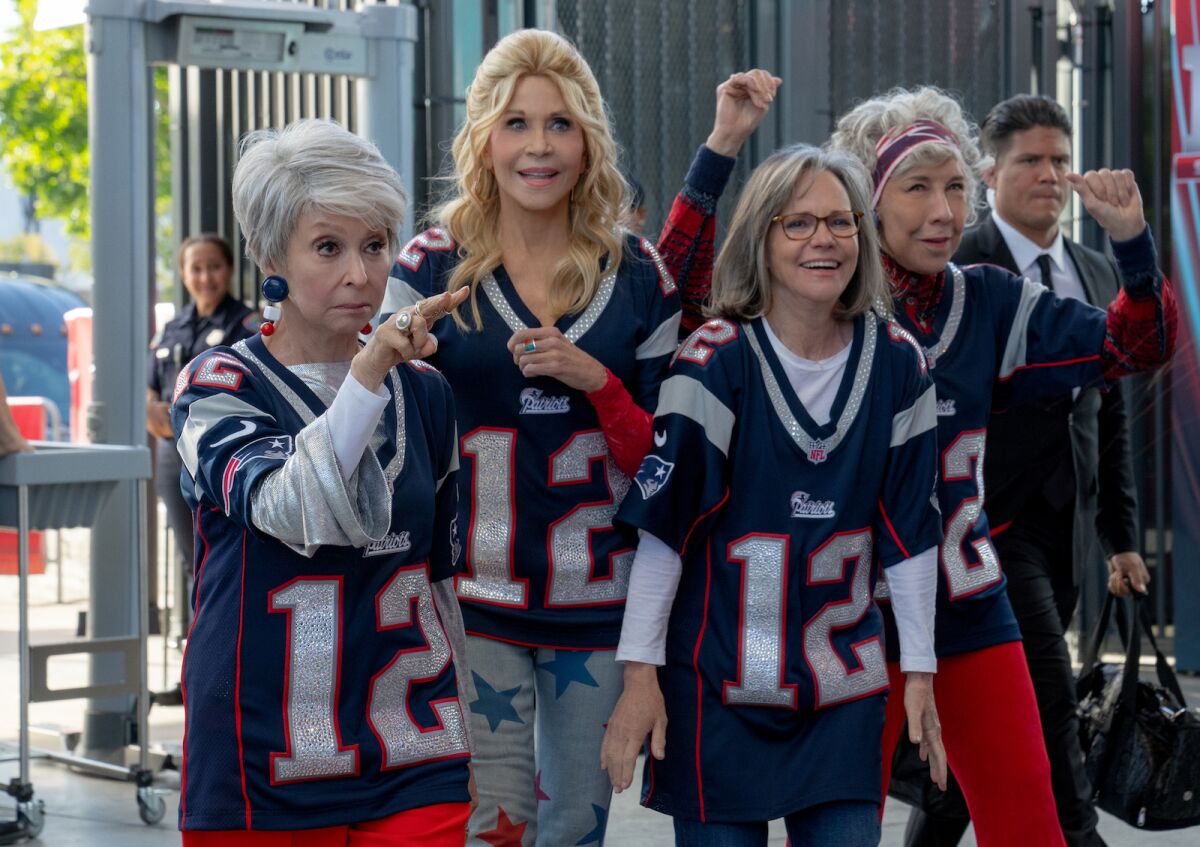 Four older women wearing number 12 New England Patriots jerseys walking into a stadium