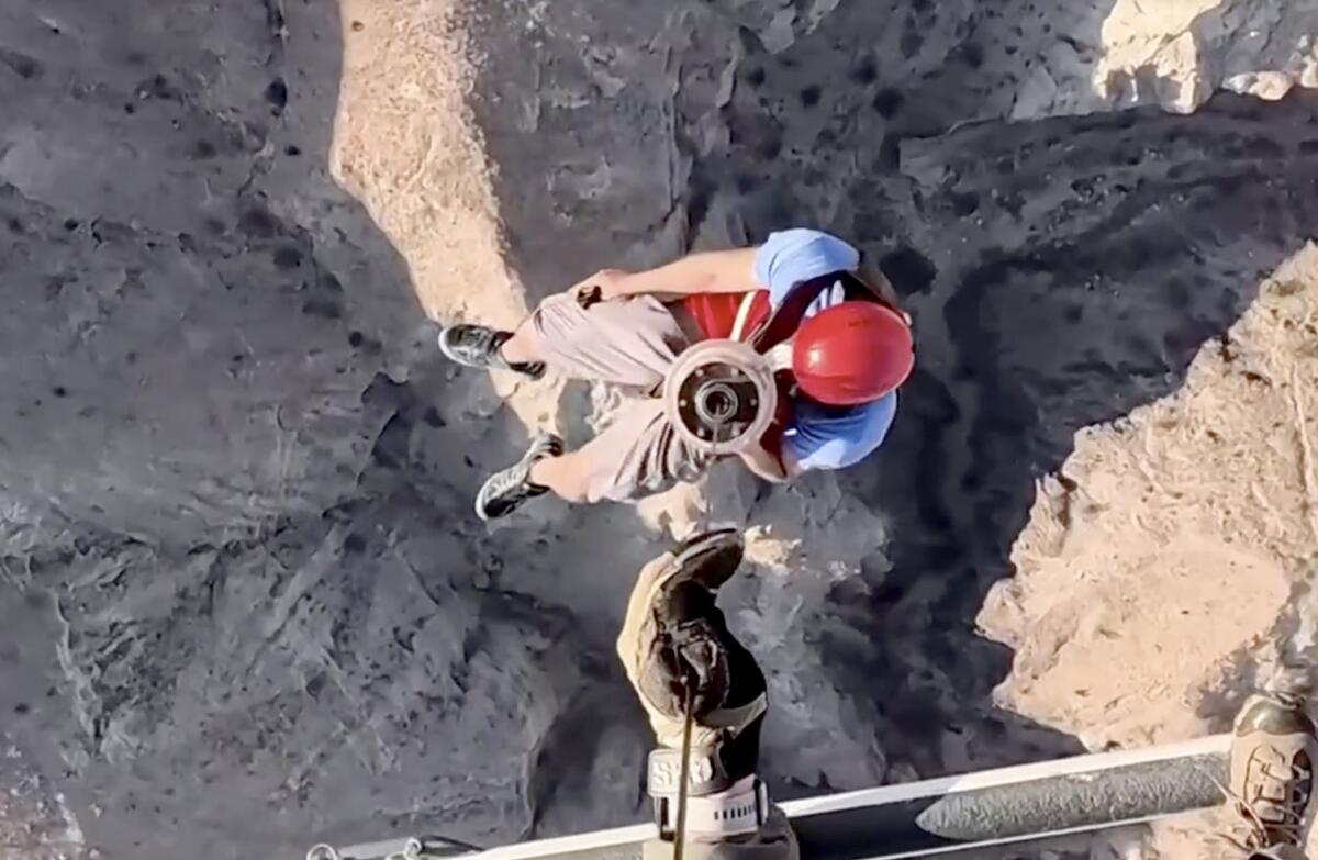 A view from above of a person in a red helmet being hoisted toward a helicopter.