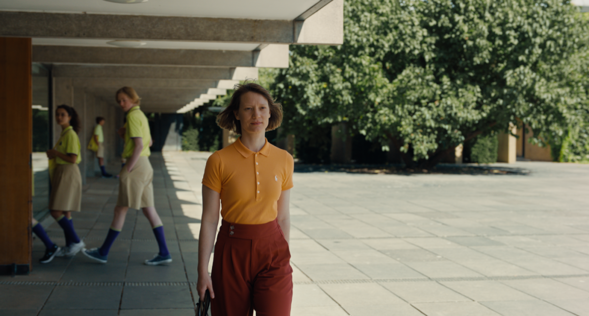 A woman in an orange shirt and red pants walks across a courtyard.
