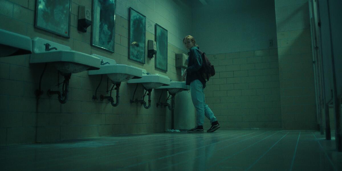 A teenage girl standing alone in a dimly lit, eerie school bathroom