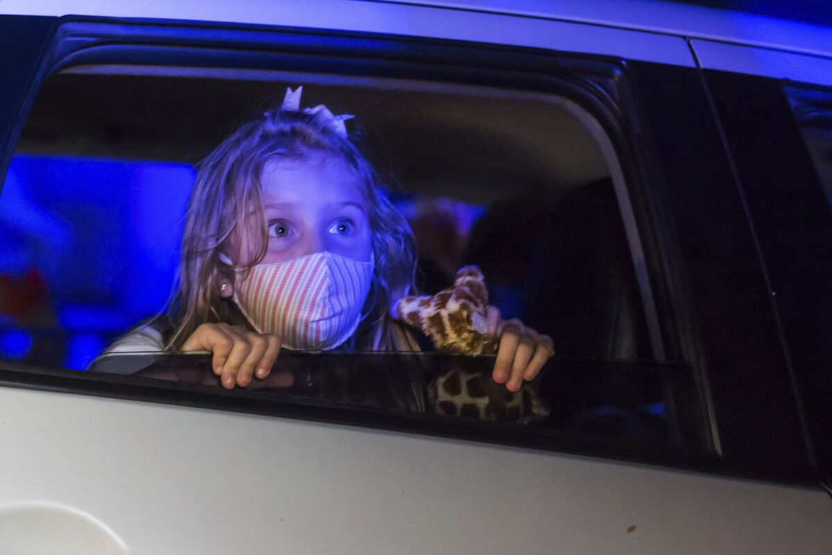 A child, wearing a protective face mask, watches a performance from inside a car, at the Hopi Hari horror theme amusement park, in the Vinhedo suburb of Sao Paulo, Brazil, Friday, Sept. 4, 2020. Due to the restrictions caused by COVID-19, the park created a drive-thru tour that allow the public to enjoy the experience by car. (AP Photo/Carla Carniel)