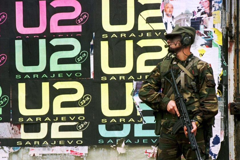A soldier stands in front of a U2 poster.
