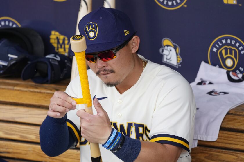 Milwaukee Brewers' Keston Hiura tapes a grip on his bat in the dugout prior to the team's spring training baseball game against the Cincinnati Reds on Sunday, March 19, 2023, in Phoenix. (AP Photo/Ross D. Franklin)