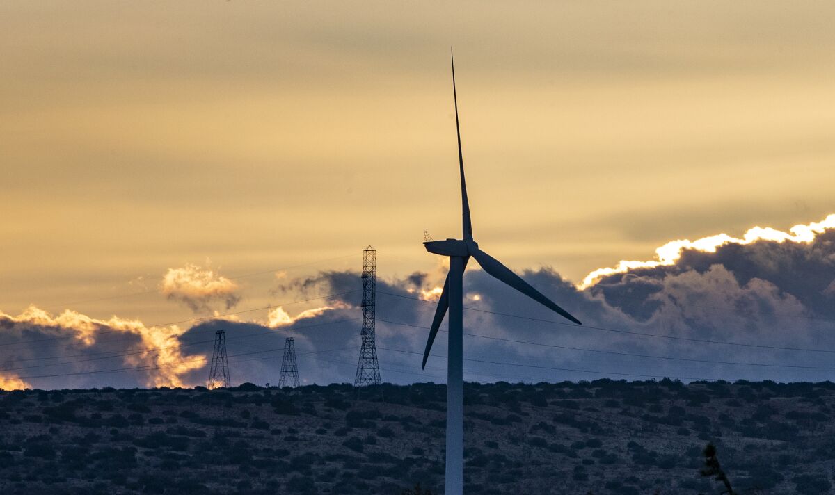 Dusk settles over wind turbines in the desert landscape with power lines and clouds in the background.