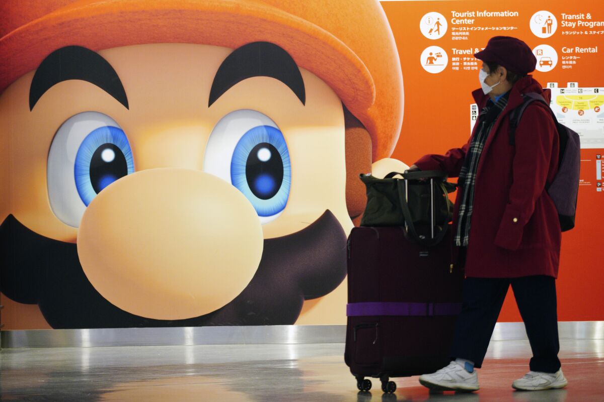 FILE - In this Jan. 23, 2020, file photo, a traveler walks past an advertisement featuring a Nintendo character at Narita airport in Narita near Tokyo. Nintendo’s profit for the nine months through December slipped 2.5%, as shortages of computer chips hurt production, the Japanese video game maker behind the Super Mario and Pokemon franchises said Thursday, Feb. 3, 2022. (AP Photo/Eugene Hoshiko, File)