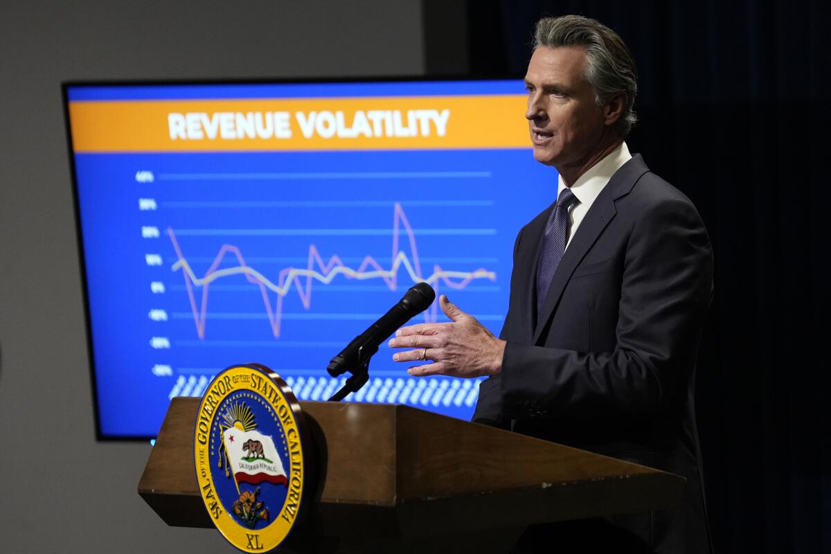 Gov. Gavin Newsom stands at a podium in front of a screen with a chart headlined "Revenue volatility."