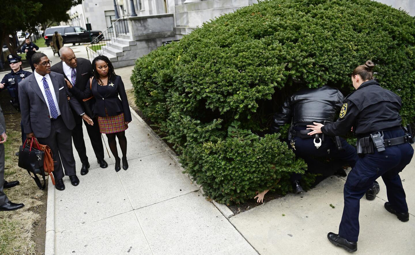 Bill Cosby, center left, arrives with spokesperson Andrew Wyatt, left, and publicist Ebonee Benson, as a protester is detained before his sexual assault trial at the Montgomery County Courthouse, Monday, April 9, 2018, in Norristown, Pa.