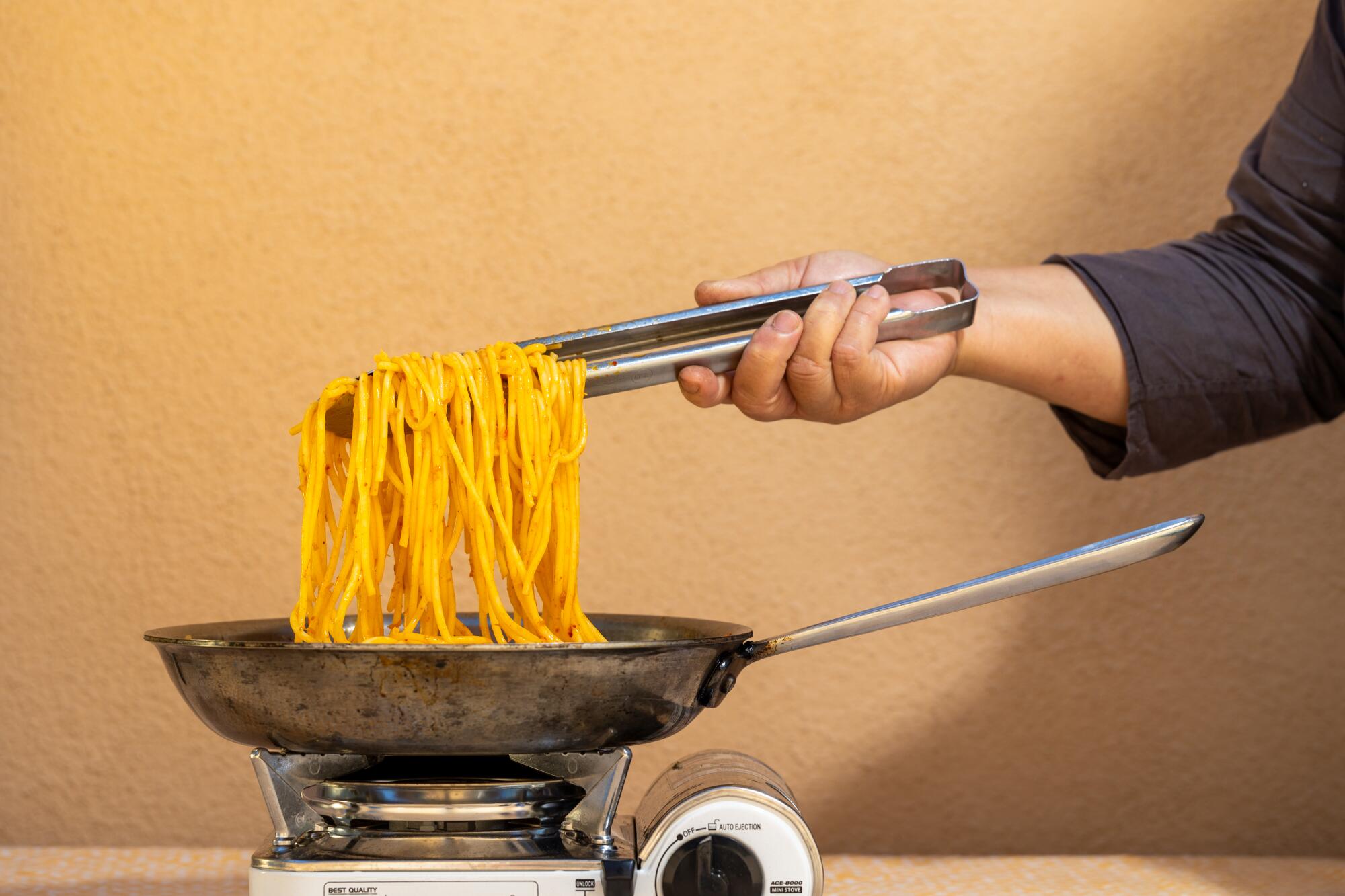 An arm reaches out and pulls spaghetti out of a pan.