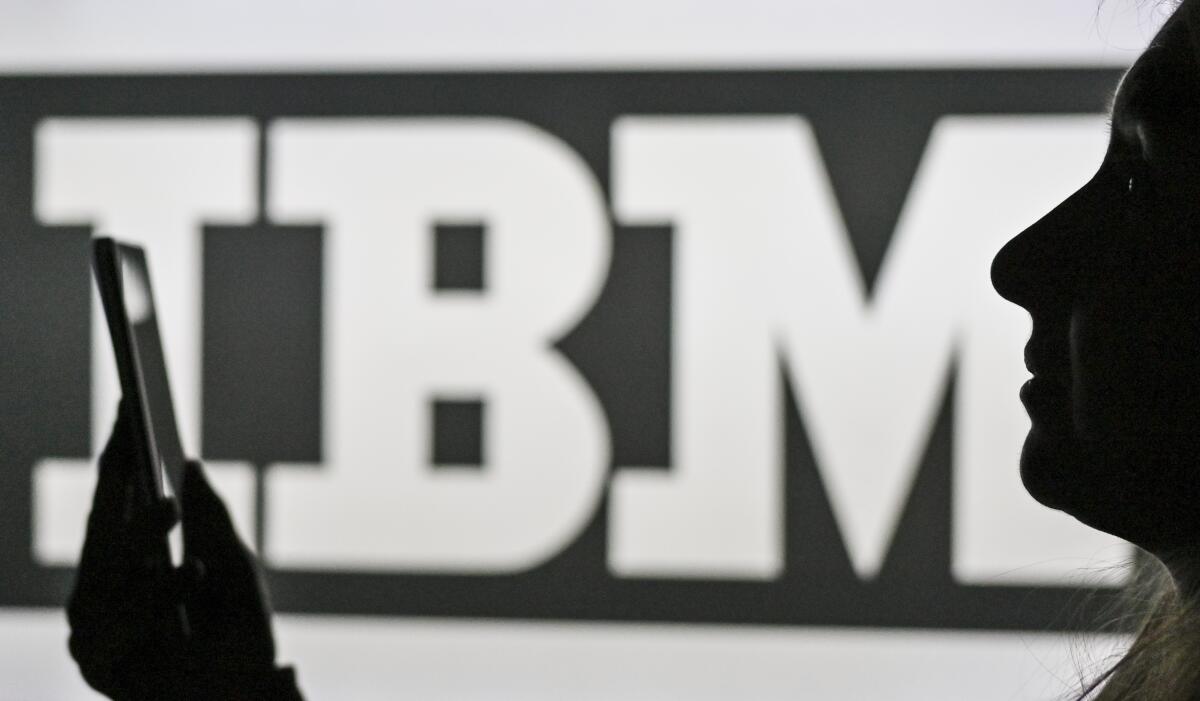 An image of a woman holding a cell phone in front of the IBM logo displayed on a computer screen.