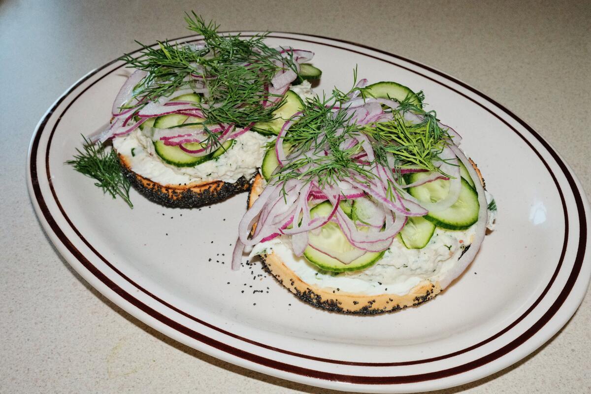 Two halves of poppy seed bagels topped with whitefish salad, dill, cucumber and onion at Belle's in Highland Park