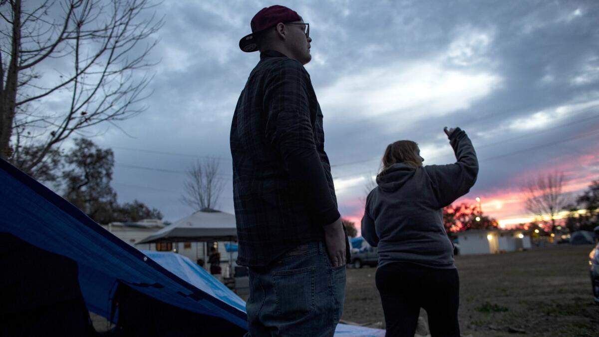 Nathan and Suzie Thomas keep an eye on approaching storm clouds after putting sandbags on a tarp covering their tents at a makeshift campground where they are staying.