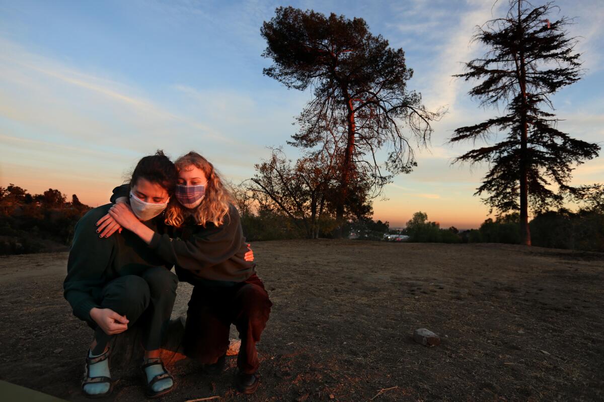 Two people wearing masks hug while sitting outside.