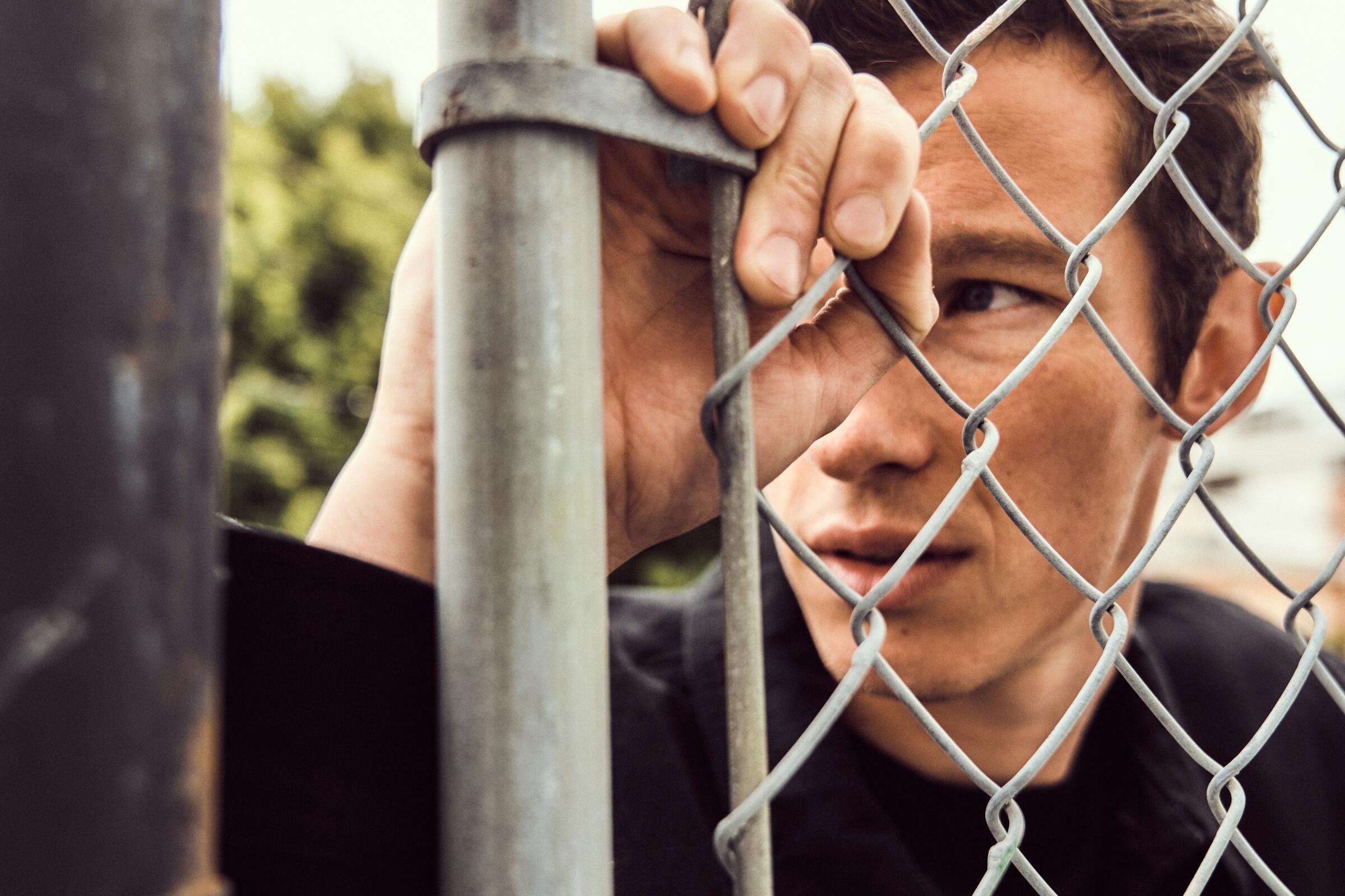 Callum Turner stands behind a chain-link fence for a portrait.