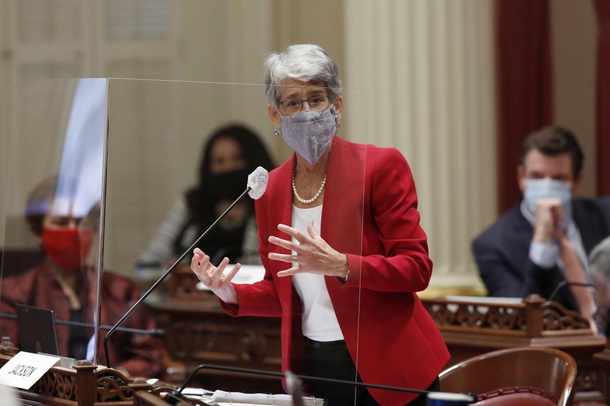 State Sen. Hannah-Beth Jackson wears a mask and speaks behind plexiglass on the floor of the California Senate