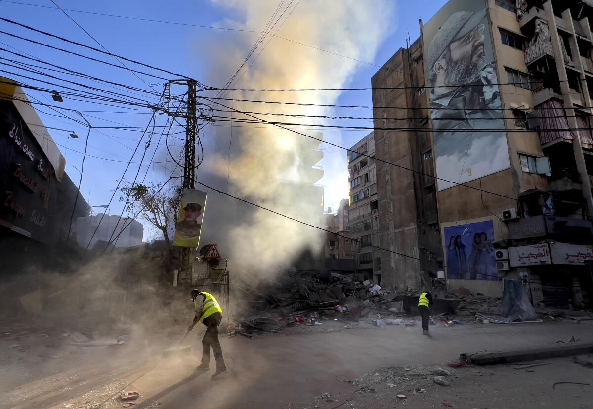 Workers clean a street as smoke rises from a destroyed building hit by an Israeli airstrike.