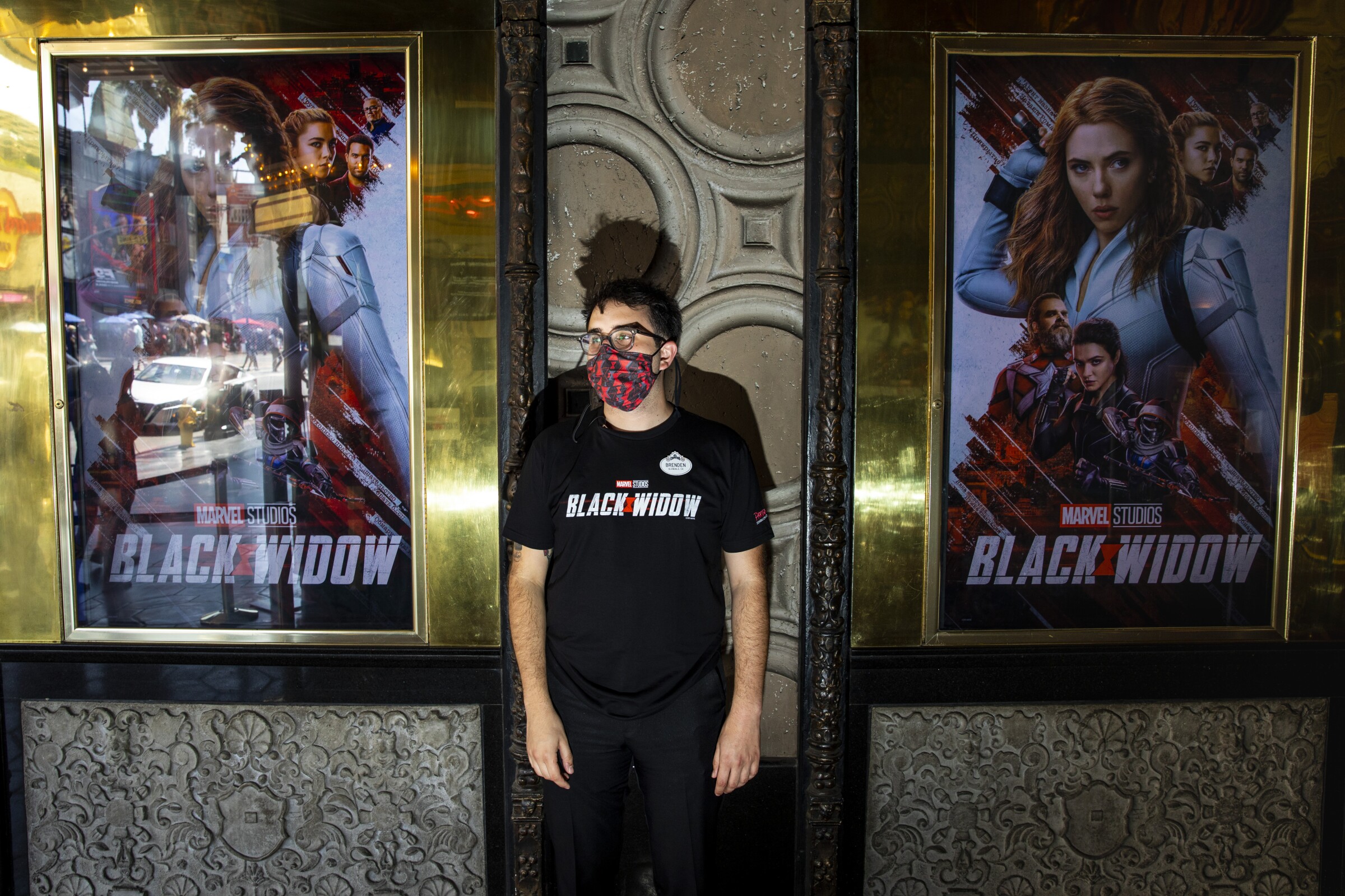 A masked young man stands between two movie posters