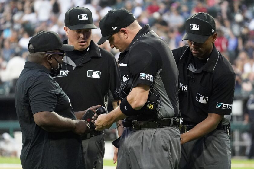 MLB Network's Kelvin Pickens, left, inspects radio and headset for a call on a play review with umpires Cory Blaser, second from left, Edwin Moscoso, right, and Dan Bellino after the first inning of a baseball game in Chicago, Friday, July 22, 2022. After a century and a half of Major League Baseball — after generations of grunts and growls, of muffled shouts and dramatic arm gestures and a cultivated sense of remoteness — something quietly extraordinary happened to the national pastime this year: The umpires began talking to the world. (AP Photo/Nam Y. Huh)
