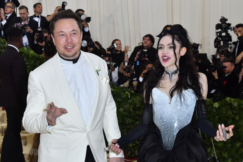 Elon Musk and Grimes speak while wearing formal attire in front of a crowd of photographers.