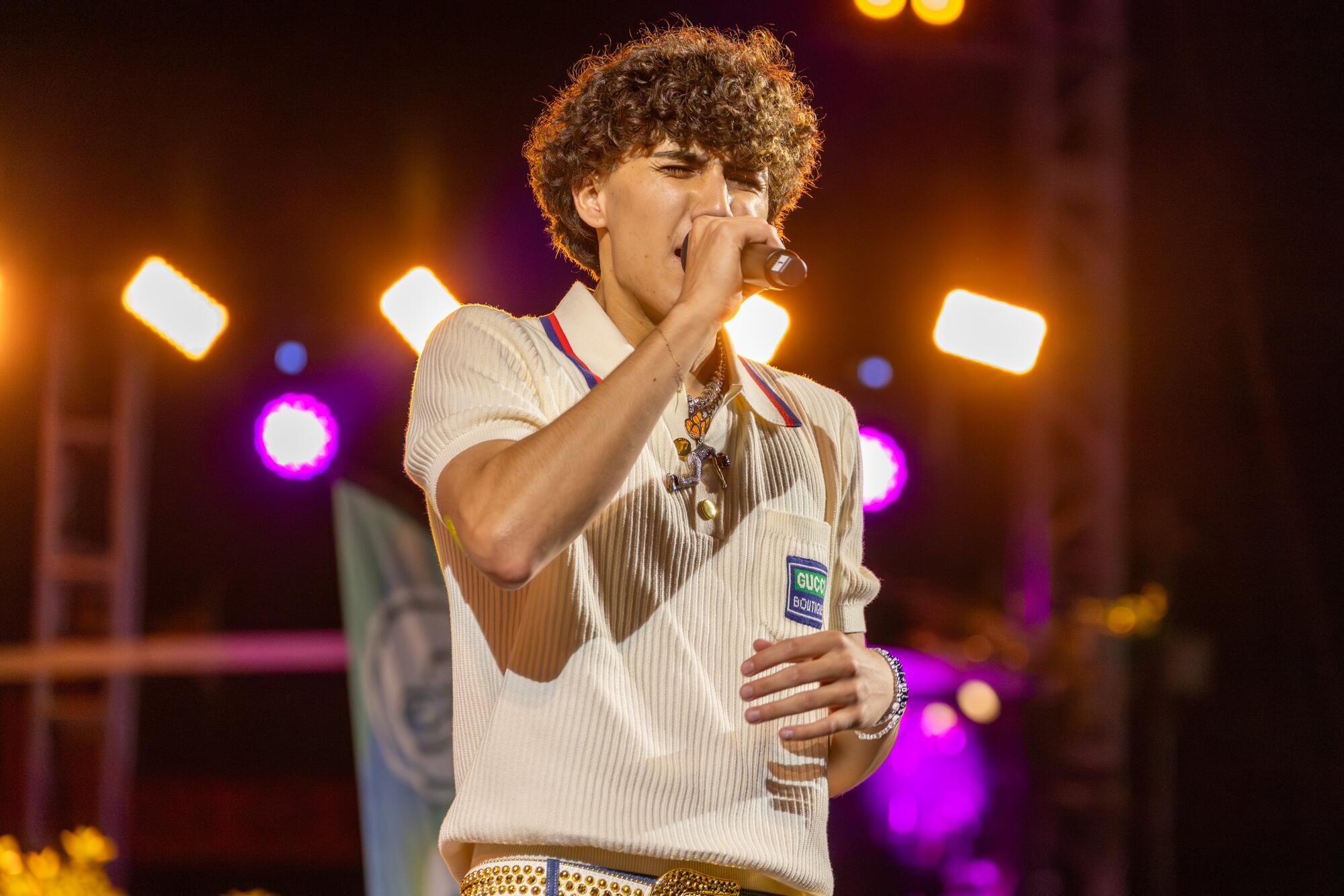 DannyLux holds a microphone to his mouth, stage lights behind him