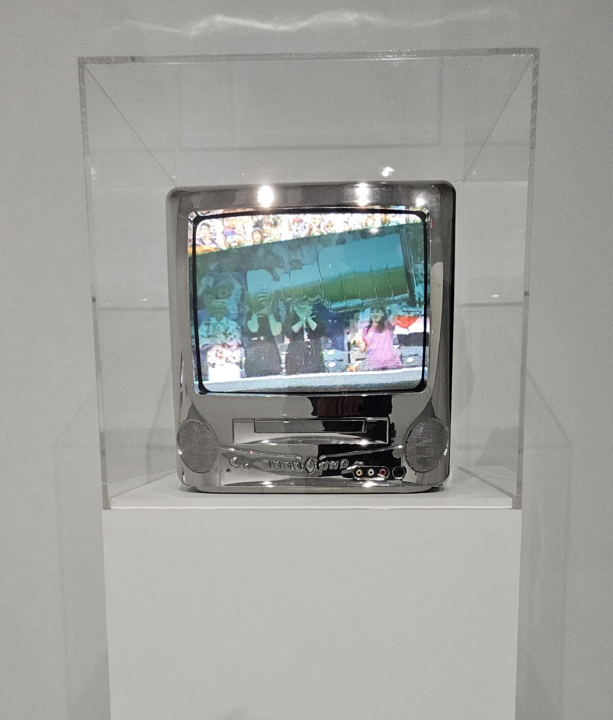 A small chrome-plated television on a pedestal, in a Plexiglass box.