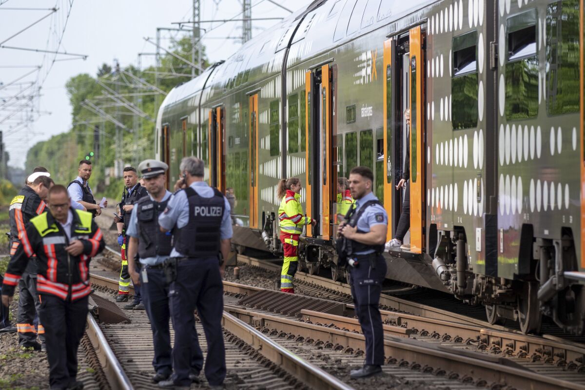 Police officers standing in front of a regional train in Herzogenrath, Germany, Friday, May 13, 2022. Three passengers on a regional train in Germany overpowered an Iraq-born man who wounded five people with a knife on Friday, authorities said. (Ralf Roeger/dpa via AP)