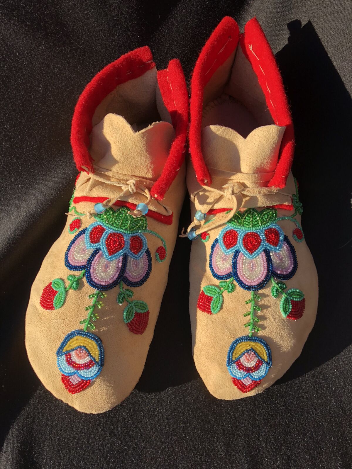 Two buckskin moccasins, hand-beaded with ornate red, pink, blue, white and yellow flowers.