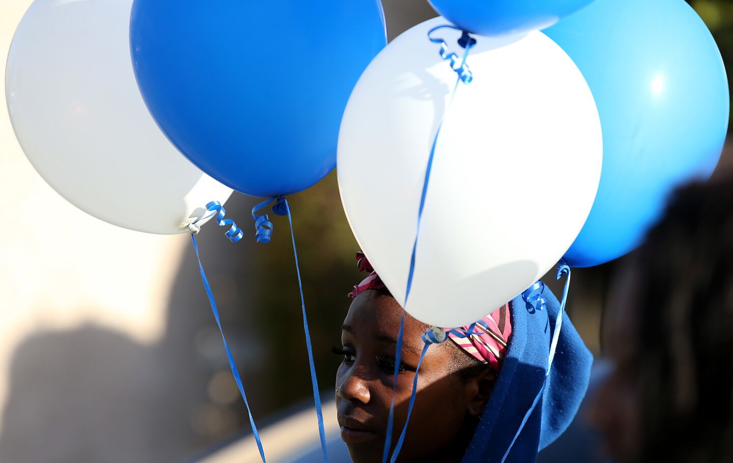 A young woman leaves blue and white balloons at a sidewalk memorial to Carnell Snell Jr. on Sunday afternoon.