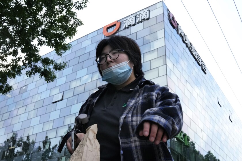 A woman walks past the headquarters for Didi Beijing on July 16, 2021. Chinese ride-hailing service Didi Global Inc. said Friday, Dec. 3, 2021 it will pull out of the U.S. stock market and shift its listing to Hong Kong as the ruling Communist Party tightens control over tech industries. (AP Photo/Ng Han Guan)