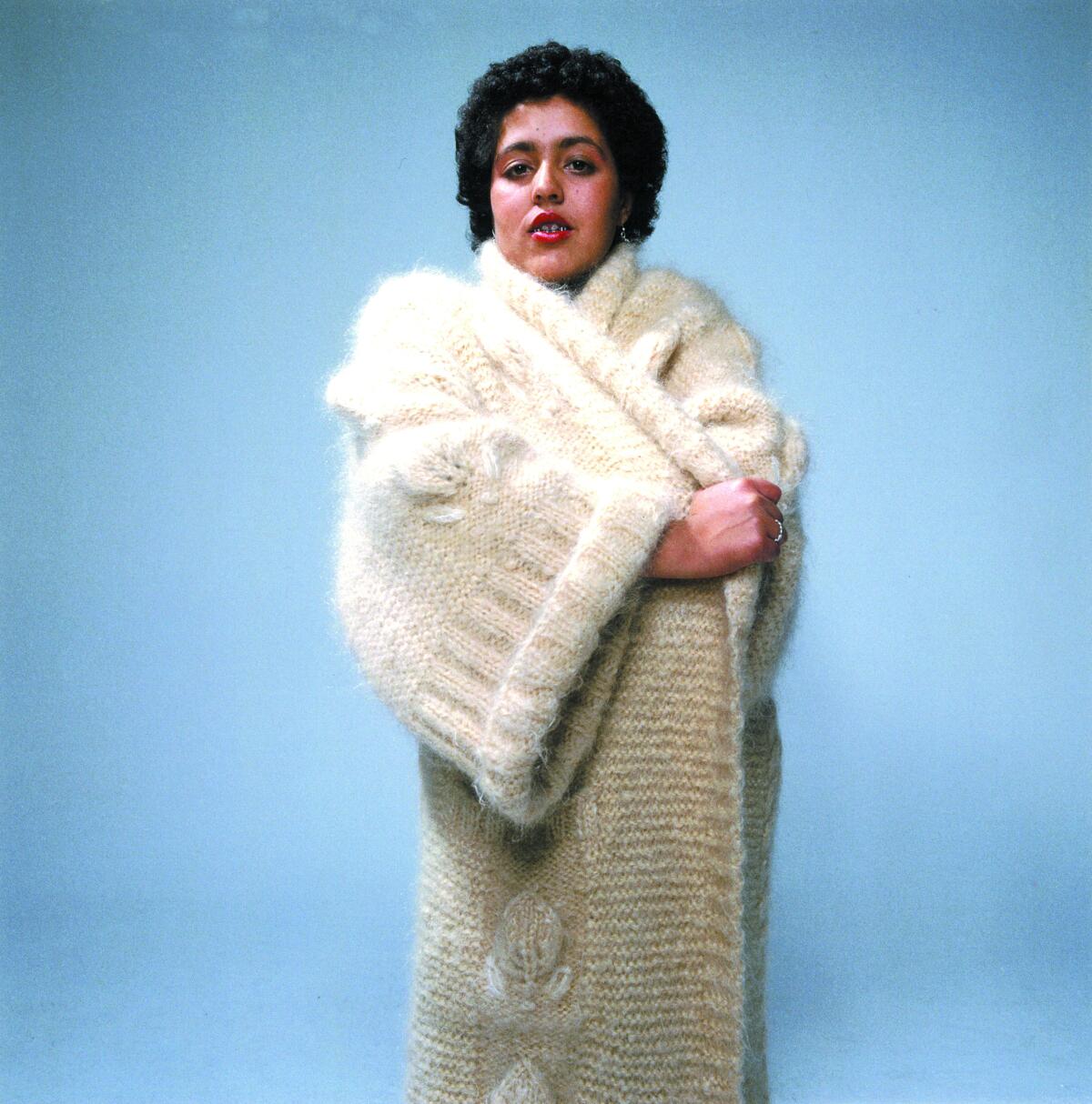 A woman wears a long white sweater.