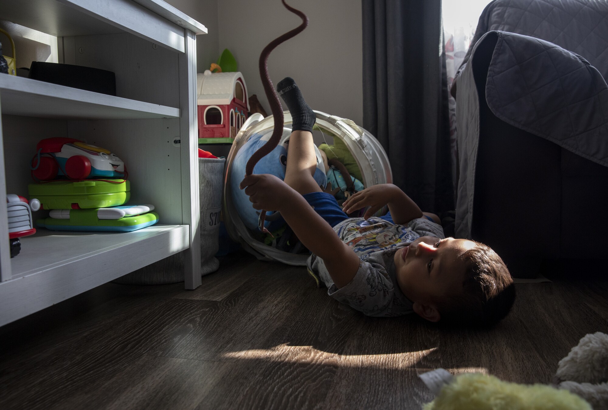 A child lies on the floor playing with a toy snake 