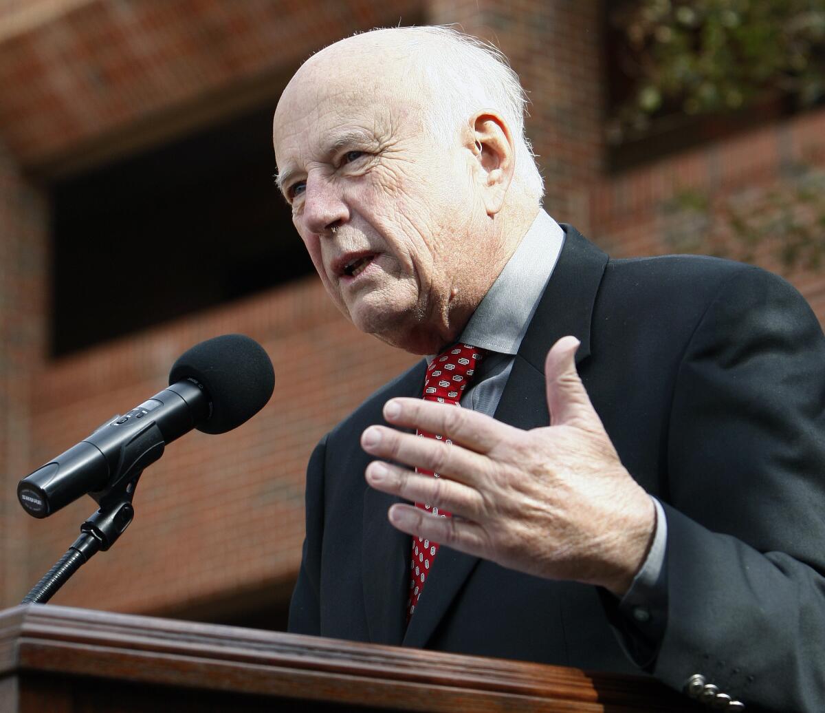 Big 12 Interim Commissioner Chuck Neinas speaks at a podium during a statue unveiling.