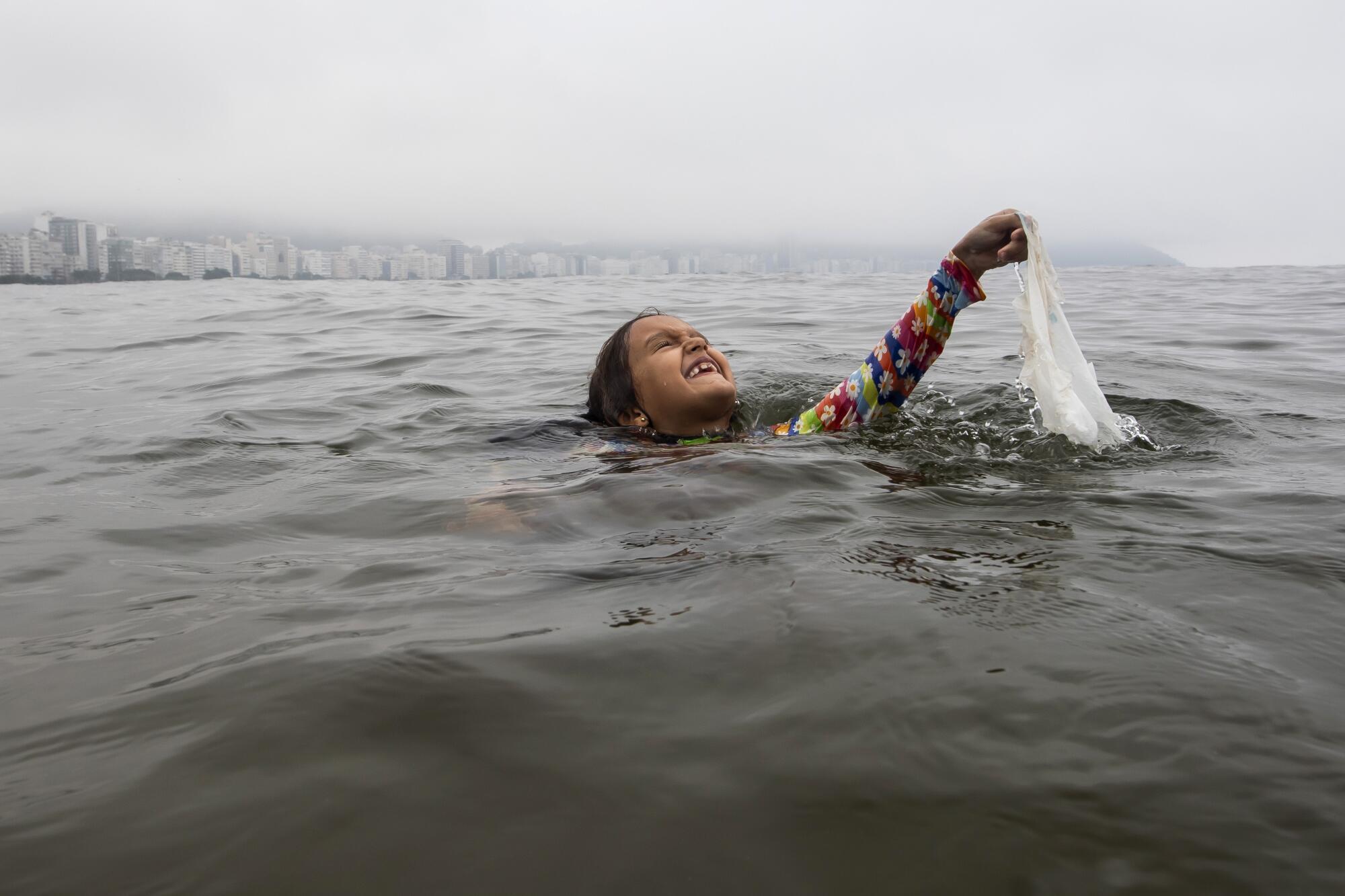 A child swimming in the ocean holds up a plastic bag.