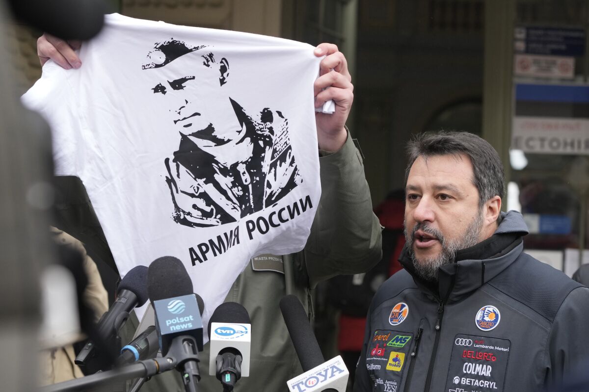 The Mayor of Przemysl, Wojciech Bakun, left, holds up a t-shirt with the likeness of Russian President Vladimir Putin and the words "The Russian Army" as Italy's League Party leader, Matteo Salvini, right, speaks with journalists outside the train station in Przemysl, Poland, Tuesday, March 8, 2022. Matteo Salvini was confronted Tuesday by the mayor of Przemysl, Wojciech Bakun, during a news conference outside the train station where many of the more than 2 million refugees from war in Ukraine have come in recent days. (AP Photo/Czarek Sokolowski)