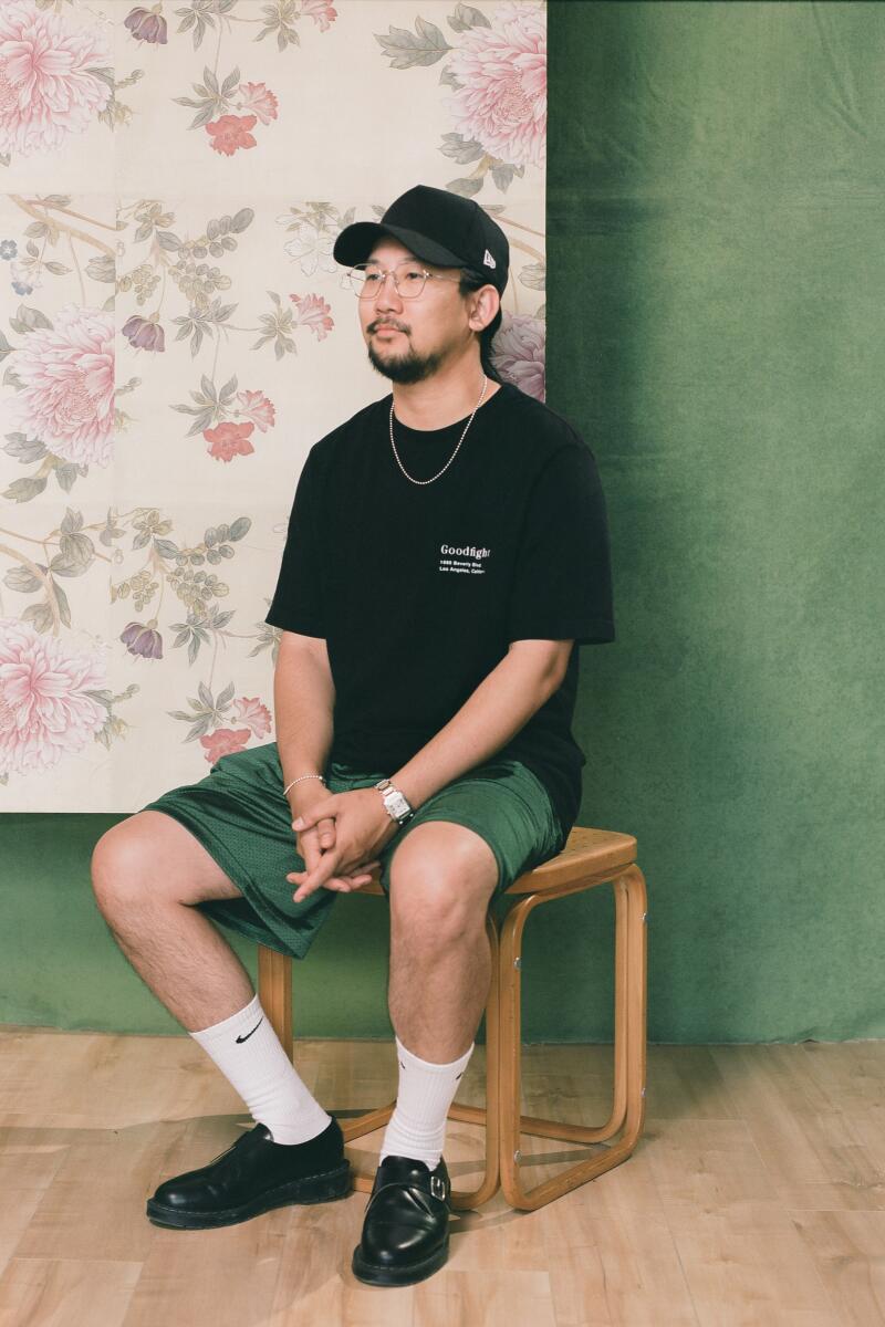 Calvin sits on a stool in front of a green and floral backdrop