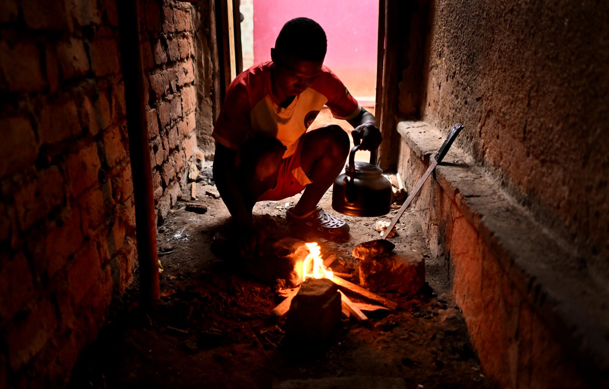 Dennis Kasumba lights a fire to make tea for his grandmother at their home in Uganda.