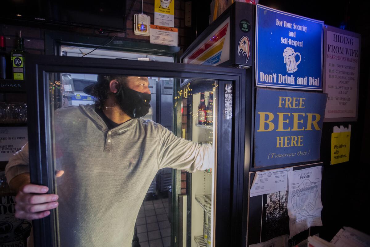 Jim Rafferty, owner of Kelly's Korner in Placentia, grabs a beverage for a customer to take out on Saturday. The sports bar is effectively grounded as the pandemic shutdown has limited it to take-out only.
