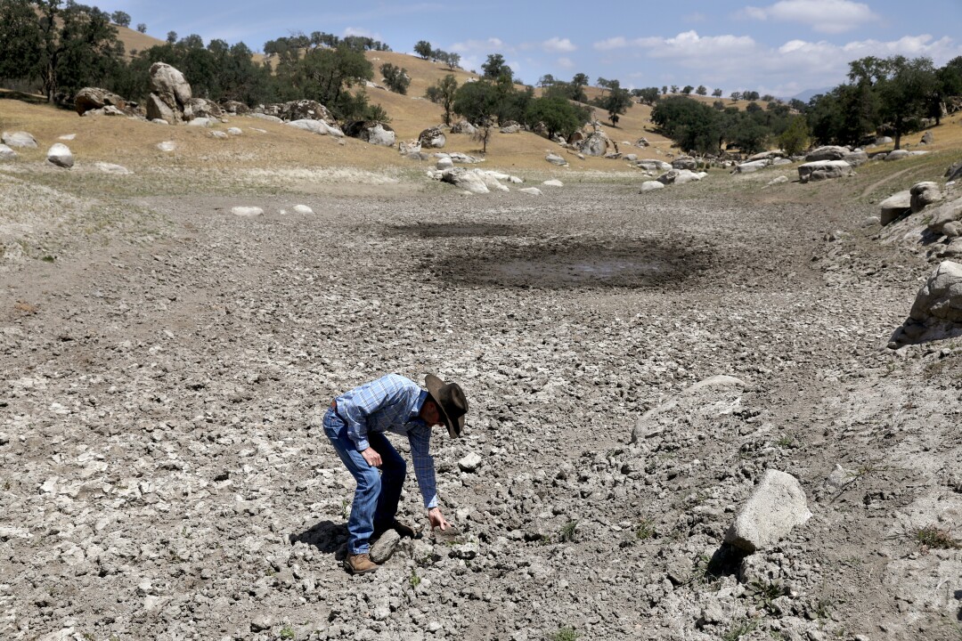 An empty reservoir with John Guthrie reaching down to the ground in it. 