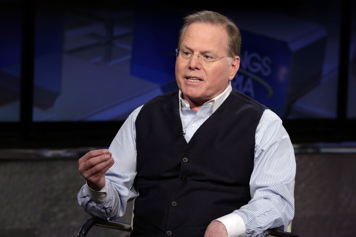 A man in a sweater vest and button-down shirt gestures as he talks.