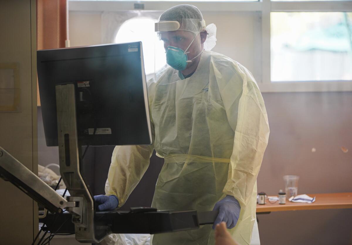 A person wearing personal protection equipment stands in front of a computer.