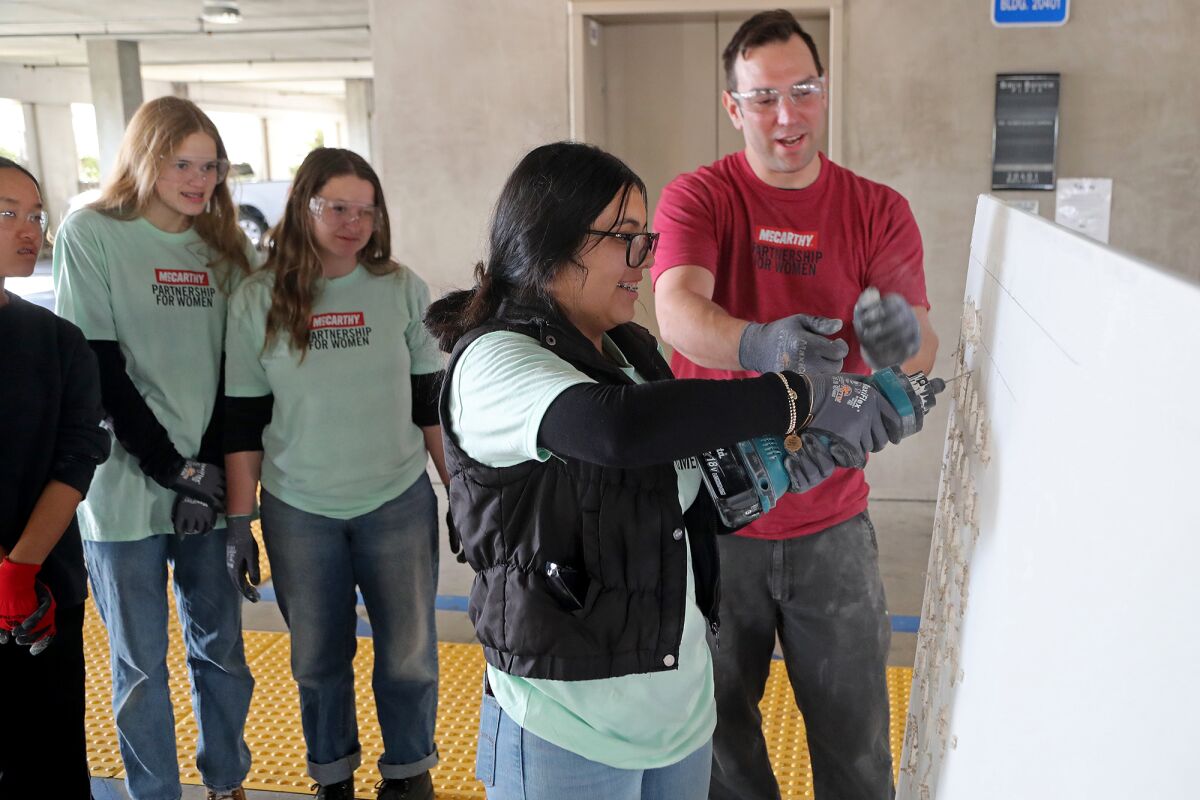 Foreman David Sandbrook encourages Chantal Jimenez to drill through drywall.