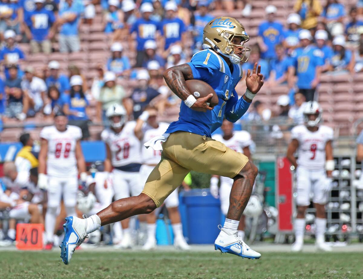 UCLA quarterback Dorian Thompson-Robinson runs with the ball as players from the sideline watch.