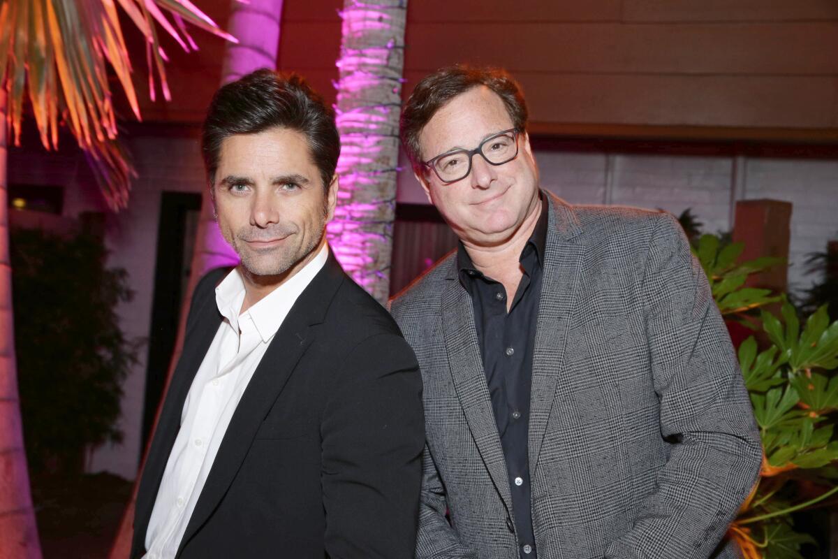John Stamos, in a black suit, stands with Bob Saget, in a gray suit, outside Hollywood's TCL Chinese Theatre in 2016