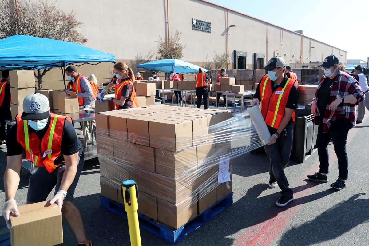Volunteers wearing safety vests help organize stacks of boxed Thanksgiving meals.