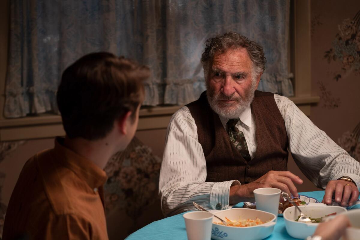A man in shirtsleeves, a vest and a tie talks to a teenager at the dinner table in "The Fabelmans."