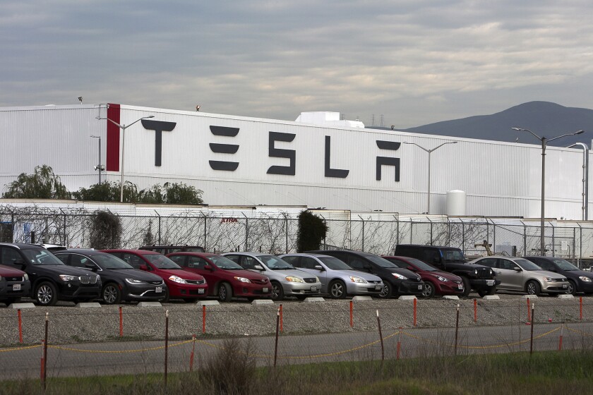A row of cars parked in front of a white building marked TESLA.