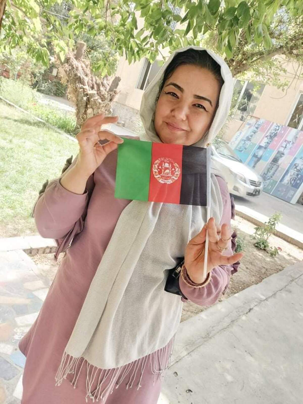 A woman in a pink outfit with white head scarf holds a green, red and black flag