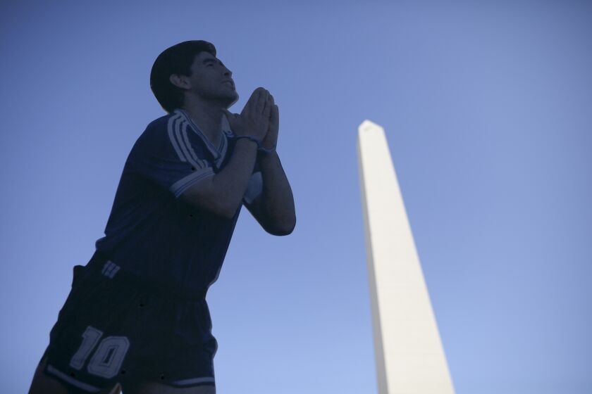 Fans of late soccer star Diego Maradona hold a cardboard cutout of Maradona at the Obelisk in Buenos Aires, Argentina, Wednesday, March 10, 2021. An investigation was opened into the circumstances surrounding Maradona's death after he passed away last November. (AP Photo/Rodrigo Abd)