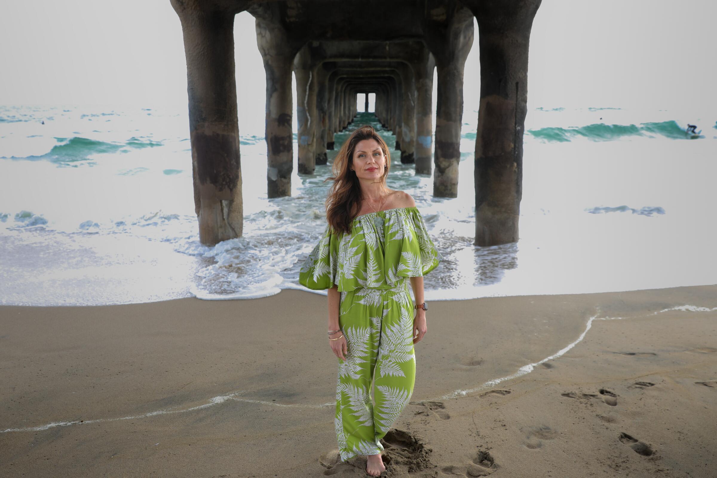 A woman in a green and white outfit stands under a pier with the ocean in the background.