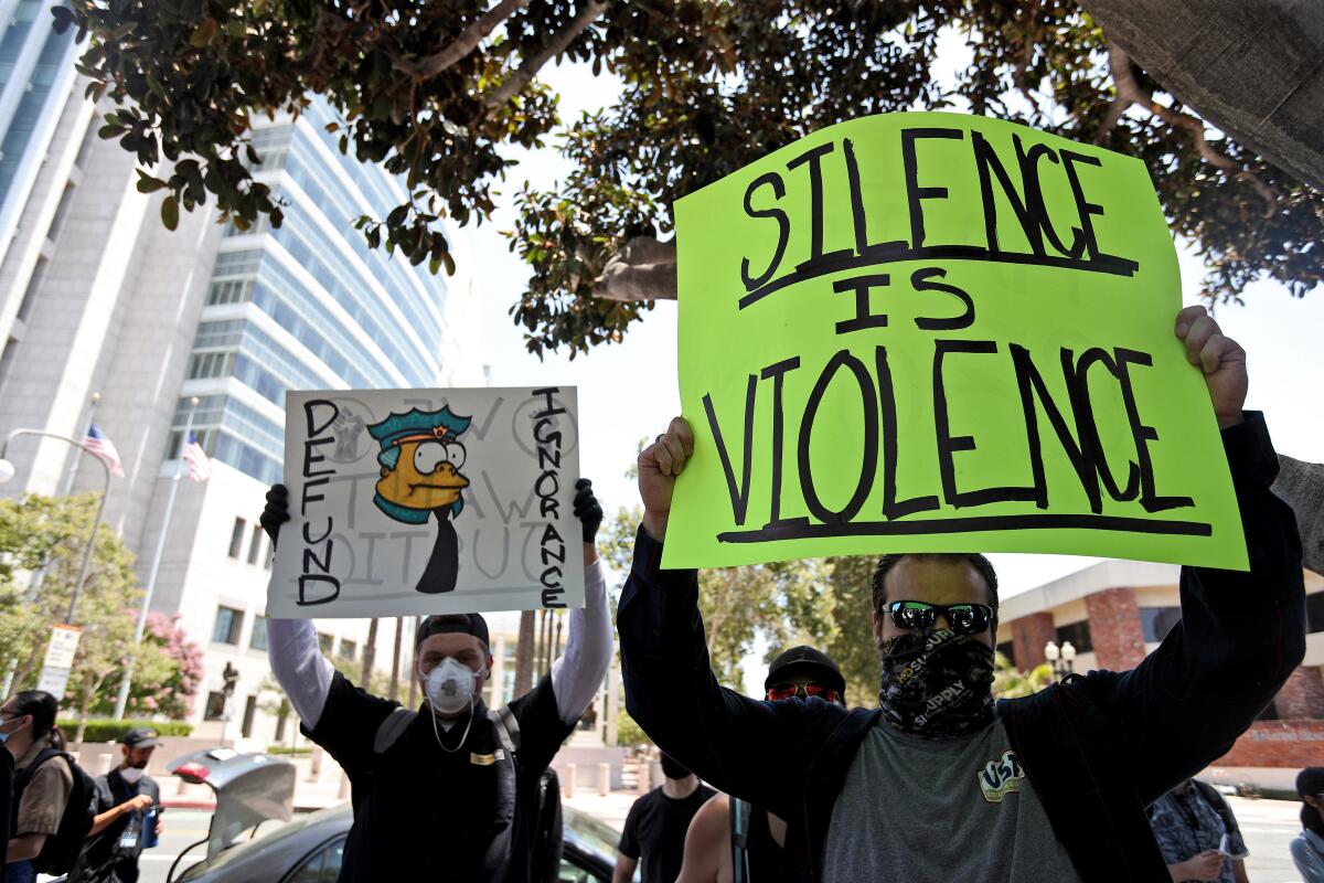 Chuck Newman, 35, of Long Beach, right, holds a sign during the Juneteenth event at Sasscer Park in Santa Ana on Friday.